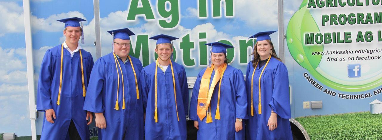 Ag students posing in front of trailer wearing graduation caps and gowns.